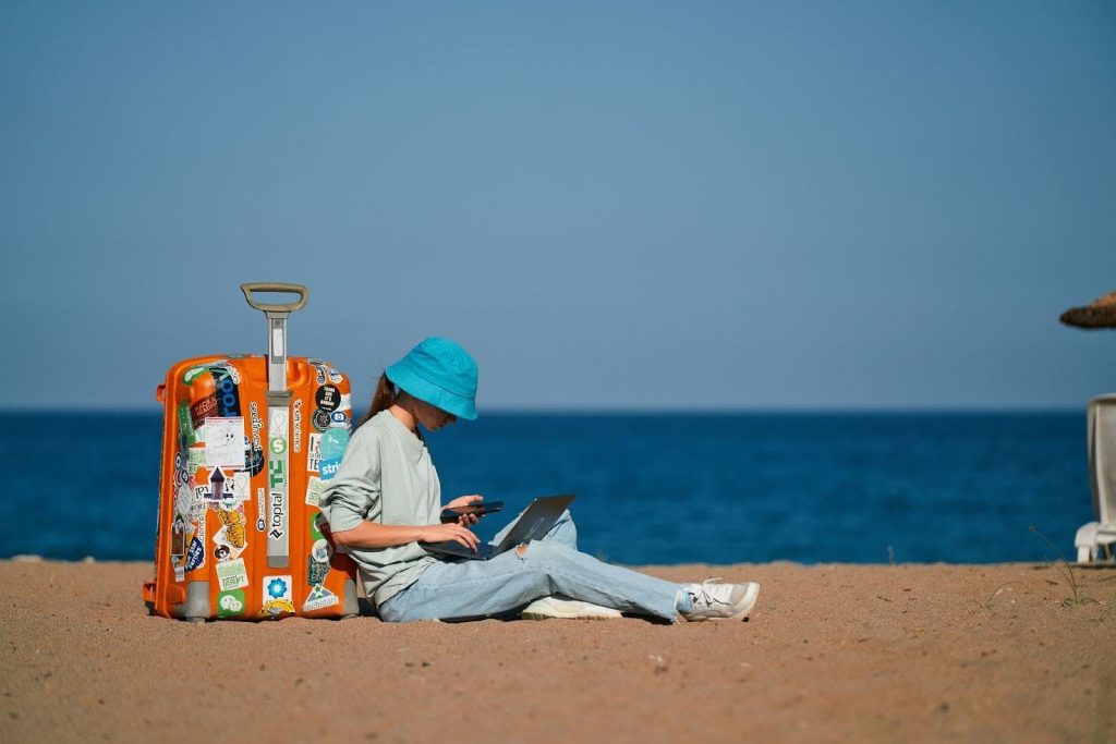 Jóven en la playa con una computadora laptop. Su propia oficina