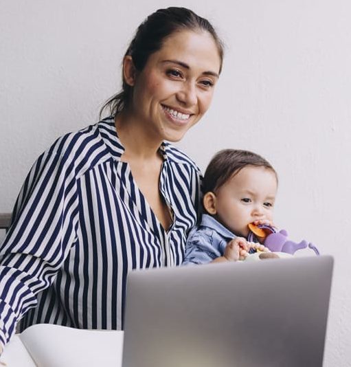 Mujer con su bebe en brazos trabajando frente a una laptop
